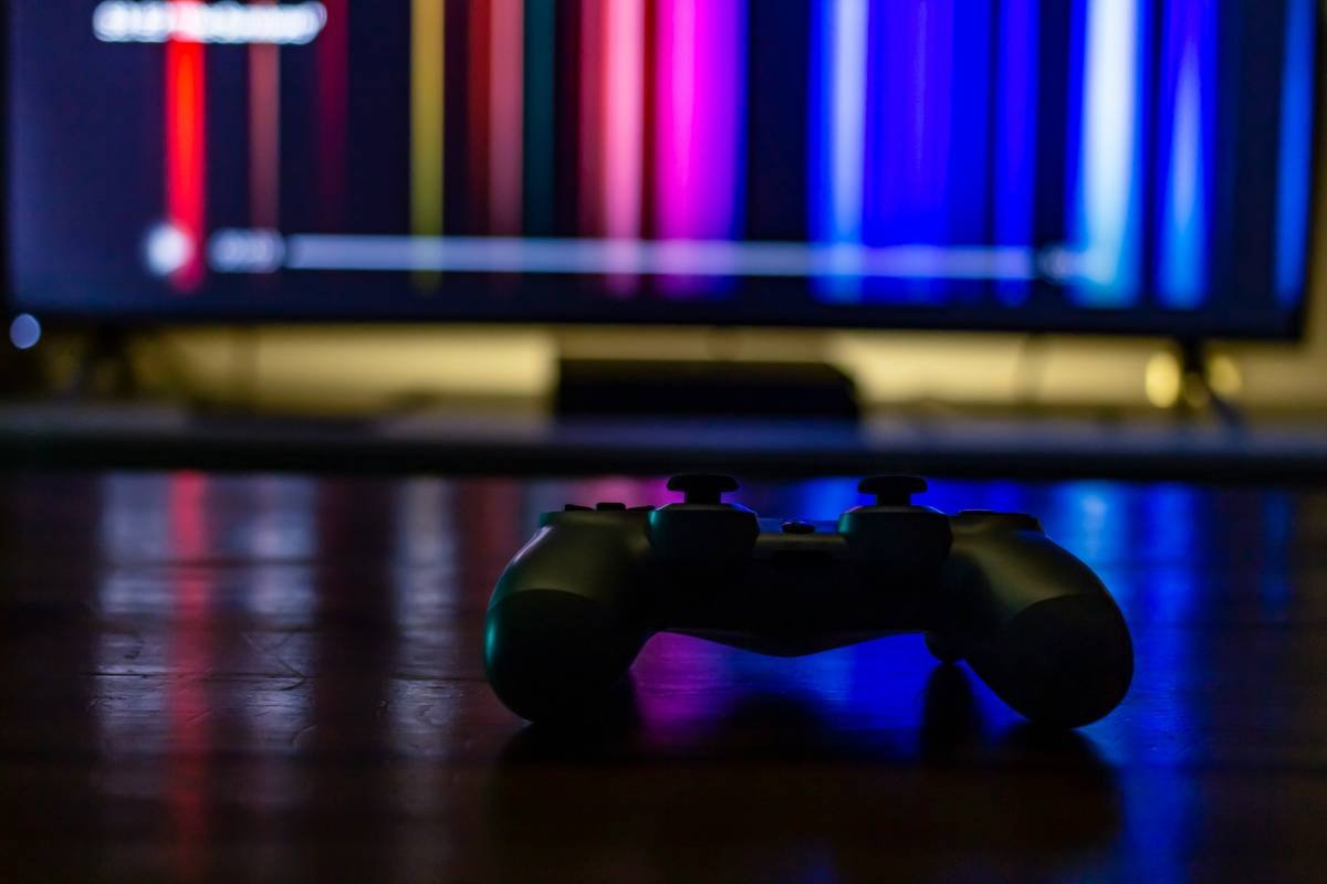 A gaming controller sitting on a coffee table with a TV in the background streaming a TV show.